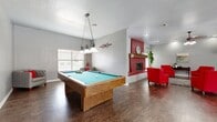 This single-floor space offers a generous and versatile layout designed to accommodate both social gatherings and professional use. The entry hallway welcomes visitors through white double doors with grid-pane windows, opening onto rich slate tile flooring that extends into several areas of the space. A ceiling fan overhead and seating along the walls create a welcoming reception atmosphere, with a corridor leading further into the interior.

The combined living, dining, and kitchen area serves as the heart of the space. The kitchen features warm wood cabinetry, dark countertops, full appliances including a refrigerator, range, and dishwasher, and slate tile flooring. French doors in the kitchen and dining areas provide direct access to an outdoor pool area, filling the space with natural light. The living area is anchored by a striking red-painted fireplace with a wood mantel, flanked by windows. Dark hardwood-style flooring flows through the living zone, which also accommodates a full-size pool table beneath a pendant light fixture.

The private office is distinguished by a bold, textured crimson accent wall, slate tile flooring, and a glass-paned interior door, offering a polished and focused environment within the broader space.