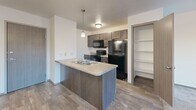 This well-designed one-bedroom, one-bathroom unit in Sioux Falls, South Dakota, offers a practical and comfortable layout across a single floor. The open-concept kitchen flows seamlessly into the living area, creating a connected and functional space. The kitchen features dark cabinetry, a peninsula with a double stainless steel sink, pendant lighting, and black appliances including a refrigerator, range, and over-the-range microwave. Wood-style flooring runs throughout the kitchen and entry areas, adding warmth to the space. Adjacent to the kitchen is a dedicated pantry with built-in shelving, offering generous storage. The living area is carpeted and ceiling fan-equipped, with a sliding glass door that opens to a private balcony overlooking the surrounding area, filling the space with natural light. The bedroom is carpeted and features a large window with outdoor views, providing a bright and airy feel. The bathroom includes a full tub and shower combo with clean white surrounds. A standout feature of this unit is the in-unit laundry room, complete with a full-size top-load washer and dryer and an overhead shelf, adding everyday convenience. Clean, neutral finishes and a thoughtful layout make this an efficient and comfortable home.