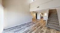 This two-story apartment at 2715 S Topeka St in Wichita, Kansas offers a well-organized layout spread across two floors. The main level serves as the social hub of the unit, featuring a spacious living room with striking high ceilings that amplify the sense of openness, durable wood-look plank flooring, and a sliding glass door fitted with vertical blinds that invites natural light. A staircase with a railing leads to the upper level, adding architectural character to the space. The kitchen is equipped with stainless steel appliances — including a refrigerator and dishwasher — complemented by gray cabinetry, a double sink, light countertops, and a window that brings in additional natural light. Both bedrooms are carpeted and feature built-in closets with rod storage. The primary bedroom includes a sliding door closet and large window with vertical blinds. The second bedroom offers a bifold closet door and a window overlooking the exterior. The upper floor, accessible via the staircase, features a vaulted, angled ceiling with a clerestory window, adding a distinctive architectural touch. The full bathroom includes a tub-shower combination with built-in wall shelving. Textured ceilings are present throughout the unit, maintaining a consistent finish across all rooms.