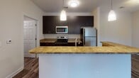 Located at 1710 Eighth Street Dr NE in Hickory, NC, this single-floor residence offers a well-designed, open-concept layout that maximizes functionality and livability. The living area is anchored by durable wood-look vinyl plank flooring in a rich gray tone, providing a modern aesthetic that flows seamlessly into the kitchen.

The kitchen serves as a central hub of the home, featuring dark espresso-finished cabinetry that extends to the ceiling for ample storage, stone-look countertops, stainless steel appliances including a refrigerator, electric range, and built-in microwave, and a peninsula with pendant lighting overhead. This open arrangement connects effortlessly to the main living space and entry area.

The bedrooms are finished with warm, plush carpeting and are equipped with ceiling fans with integrated lighting. Natural light enters through blinded windows, offering views of the surrounding neighborhood. The neutral wall tones throughout create a calm, versatile backdrop.

The bathrooms are appointed with wood-look vinyl plank flooring, dark vanity cabinetry with light countertops, and full tub/shower combinations featuring white tile surrounds and brushed nickel fixtures, including a curved shower rod and grab bar. The overall design is clean, cohesive, and move-in ready.