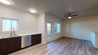 This single-floor unit located in Stockton, California, presents a clean, contemporary design throughout. Light wood-style flooring extends across all living areas, creating a cohesive and bright aesthetic that complements the neutral white walls.

The kitchen is well-appointed with a full suite of stainless steel appliances, including a gas range, over-the-range microwave, refrigerator, and dishwasher. Dark espresso-toned cabinetry with sleek hardware provides ample upper and lower storage, while light countertops offer functional workspace. The kitchen opens directly into the living area, promoting an efficient, open-concept flow.

The living area benefits from natural light via a windowed exterior door that leads to an outdoor space. A ceiling fan overhead adds both comfort and practicality. A low partition wall subtly defines areas within the open layout without interrupting the sense of spaciousness.

The bathroom features a tub-shower combination with built-in shelving, a vanity with warm-toned countertop and white cabinetry, and wood-style flooring consistent with the rest of the unit. Brushed metal fixtures and accessories complete the space with a polished finish. Overall, the unit offers a modern, functional living environment.