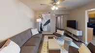This single-floor residence offers a thoughtfully designed layout that balances comfort and functionality. The living room serves as the heart of the home, featuring rich hardwood-style flooring, a ceiling fan with integrated lighting, and a neutral color palette that creates a welcoming atmosphere. The space is furnished with a plush sofa, accent seating, and a patterned area rug, complemented by a large statement artwork that adds a bold focal point.

Adjacent to the living area, the dining nook is bright and inviting, with two windows dressed in white blinds that allow natural light to filter in. A round white table paired with black chairs sits beneath a stylish pendant light, creating an intimate setting for meals.

The kitchen is equipped with warm honey-toned cabinetry, a double stainless steel sink, laminate countertops, and black appliances including a refrigerator and range, providing all the essentials for home cooking.

The primary bedroom features plush carpeting, a ceiling fan, a natural light-filled window, and understated furnishings. The second bedroom, also carpeted with a ceiling fan, comfortably accommodates twin beds. Both bathrooms are finished with wood-tone vanities, granite-style countertops, and tub-shower combinations with hardwood-style flooring, offering a clean and cohesive aesthetic throughout.
