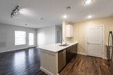 This single-story residence on Princeton Way in Dover, New Hampshire offers a thoughtfully designed open-concept layout that seamlessly connects the kitchen and living areas. The kitchen serves as a central focal point, anchored by a peninsula with a white quartz countertop and double stainless steel sink. Dark espresso lower cabinetry contrasts cleanly with bright white upper cabinets that extend to the ceiling, maximizing storage. Stainless steel appliances, including a refrigerator, range, and microwave, complete the modern kitchen setup. Wood-style flooring runs throughout the main living areas, adding warmth and durability, while recessed lighting and a track light fixture provide ample illumination.

The living area benefits from natural light through a window and glass door leading to an outdoor area. The bedroom features plush carpeting, two windows with outdoor views, and a closet with built-in shelving. The full bathroom is finished with light tile flooring, a tub-shower combination with white tile surround, and convenient built-in open shelving for storage. An in-unit laundry area is also accessible off the kitchen corridor, adding everyday practicality to this clean, contemporary residence.