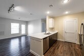 This single-story residence on Princeton Way in Dover, New Hampshire offers a thoughtfully designed open-concept layout that seamlessly connects the kitchen and living areas. The kitchen serves as a central focal point, anchored by a peninsula with a white quartz countertop and double stainless steel sink. Dark espresso lower cabinetry contrasts cleanly with bright white upper cabinets that extend to the ceiling, maximizing storage. Stainless steel appliances, including a refrigerator, range, and microwave, complete the modern kitchen setup. Wood-style flooring runs throughout the main living areas, adding warmth and durability, while recessed lighting and a track light fixture provide ample illumination.

The living area benefits from natural light through a window and glass door leading to an outdoor area. The bedroom features plush carpeting, two windows with outdoor views, and a closet with built-in shelving. The full bathroom is finished with light tile flooring, a tub-shower combination with white tile surround, and convenient built-in open shelving for storage. An in-unit laundry area is also accessible off the kitchen corridor, adding everyday practicality to this clean, contemporary residence.