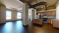 This 1-bedroom, 1-bathroom urban loft showcases a distinctive industrial aesthetic throughout its well-appointed single-floor layout. Polished dark concrete floors run seamlessly across the entire unit, complemented by soaring ceilings with exposed ductwork and track lighting that reinforce the loft's modern character. Structural columns punctuate the expansive open-plan living area, adding architectural interest while defining natural zones within the space.

The kitchen is well-equipped with warm wood cabinetry, granite countertops, stainless steel appliances including a refrigerator, range, microwave, and dishwasher, and a central island that provides additional prep space and casual seating. Pendant lighting adds a refined touch overhead.

The generously sized bedroom features large windows that frame views of the surrounding cityscape, flooding the room with natural light. Two spacious closets with built-in shelving and hanging rods offer ample storage. The full bathroom is finished with tile flooring, a granite-topped vanity with a large mirror, and a tub-shower combination enclosed by glass sliding doors.

Throughout the unit, wall sconces and large windows ensure a bright, welcoming atmosphere, while the urban views and industrial design elements create a dynamic, contemporary living environment.