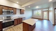 This efficient and thoughtfully designed one-bedroom, one-bathroom unit offers a functional layout across a single floor. The kitchen serves as a focal point of the living space, showcasing rich dark wood cabinetry, light-toned countertops, a central island ideal for meal prep or casual dining, and a full suite of stainless steel appliances including a refrigerator, range, microwave, and dishwasher. Recessed lighting illuminates the kitchen and flows into the adjacent living area, which features warm hardwood-style flooring and a large window that frames lush outdoor greenery, filling the space with natural light.

The bedroom is a comfortable retreat, carpeted for warmth and featuring impressively tall ceilings with an elevated window arrangement that maximizes both light and privacy. Views of mature trees add a serene, natural backdrop to the room.

The bathroom is clean and modern, outfitted with dark wood cabinetry, a wide vanity with a light countertop, a large mirror with overhead lighting, tile backsplash accents, and hardwood-style flooring. The overall design palette throughout the unit is neutral and cohesive, combining warm wood tones with light walls to create a welcoming and move-in-ready living environment.