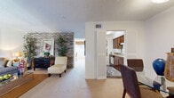 This thoughtfully designed single-floor residence offers a practical and comfortable layout encompassing a bedroom, bathroom, combined living and dining room, kitchen, pantry, dedicated office space, and three closets. The open living and dining area is a standout feature, highlighted by a striking exposed brick accent wall that adds texture and character to the space. Soft carpeting flows throughout the main living areas, while large windows dressed with elegant drapes invite natural light and provide pleasant outdoor views. The kitchen is efficiently laid out with warm wood cabinetry, light countertops, a stainless steel sink, dishwasher, and dark hardwood-style flooring, complemented by an adjacent pantry for added storage. The bedroom is a serene retreat, featuring carpeted floors, a window with ample natural light, and generous closet access. A dedicated office nook provides a quiet workspace with its own window and neutral finishes. The bathroom includes a soaking tub, single-sink vanity with white cabinetry, and rich hardwood-style flooring. Three closets throughout ensure abundant storage. The textured ceilings add a classic architectural detail consistent throughout the space, creating a cohesive and welcoming atmosphere overall.