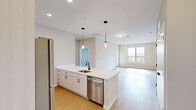 Located at 55 Seely School Dr in Groton, CT, this thoughtfully designed 2-bedroom, 2-bathroom residence offers a clean, contemporary aesthetic throughout its well-appointed single floor. The open-concept layout seamlessly connects the kitchen, dining, and living areas, creating a bright and airy communal space bathed in natural light from large windows. The kitchen is a standout feature, anchored by a generous island with a crisp white quartz countertop, white shaker cabinetry, a matte black faucet, and stainless steel appliances including a dishwasher and refrigerator. Stylish pendant lighting above the island adds a modern touch. Light-toned hardwood-style flooring flows throughout the main living areas, complementing the neutral color palette. The living room opens to a private balcony, extending the living space outdoors. Both bedrooms are carpeted for comfort, with the spacious primary bedroom featuring a walk-in closet equipped with wire shelving. The bathrooms are finished with marble-look tile flooring, wood-toned vanities, white countertops, and matte black fixtures. Additional conveniences include four closets, a dedicated laundry area, and a welcoming entrance, making this residence as functional as it is refined.