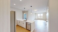 Located at 55 Seely School Dr in Groton, CT, this thoughtfully designed 2-bedroom, 2-bathroom residence offers a clean, contemporary aesthetic throughout its well-appointed single floor. The open-concept layout seamlessly connects the kitchen, dining, and living areas, creating a bright and airy communal space bathed in natural light from large windows. The kitchen is a standout feature, anchored by a generous island with a crisp white quartz countertop, white shaker cabinetry, a matte black faucet, and stainless steel appliances including a dishwasher and refrigerator. Stylish pendant lighting above the island adds a modern touch. Light-toned hardwood-style flooring flows throughout the main living areas, complementing the neutral color palette. The living room opens to a private balcony, extending the living space outdoors. Both bedrooms are carpeted for comfort, with the spacious primary bedroom featuring a walk-in closet equipped with wire shelving. The bathrooms are finished with marble-look tile flooring, wood-toned vanities, white countertops, and matte black fixtures. Additional conveniences include four closets, a dedicated laundry area, and a welcoming entrance, making this residence as functional as it is refined.