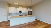 Located at 1538 W 28th St in Cleveland's vibrant Ohio City neighborhood, this single-floor residence offers a thoughtfully designed open-concept layout with contemporary finishes throughout. The expansive living and kitchen area serves as the heart of the home, featuring warm hardwood flooring, recessed lighting, and a glass-paneled entry door that draws in natural light. The kitchen is a standout, outfitted with white shaker-style cabinetry, a light blue glass tile backsplash, stainless steel appliances including a range, microwave, and French door refrigerator, and a generous island with a undermount sink and pendant globe lighting above — ideal for both cooking and entertaining. The bedrooms are carpeted and bathed in natural light from large windows fitted with horizontal blinds, offering pleasant outdoor views of the surrounding neighborhood greenery and cityscape. The bathroom is clean and modern, featuring a white vanity with ample storage, a large mirror, and tile flooring. A spacious walk-in closet with wire shelving provides generous storage. Neutral warm-gray tones and clean lines throughout the space create a cohesive, move-in-ready aesthetic suited for contemporary urban living.