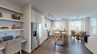 This thoughtfully designed single-floor residence offers a seamless blend of modern finishes and comfortable living. The open-concept kitchen is a standout feature, showcasing white shaker cabinetry extending to the ceiling, granite countertops, a classic subway tile backsplash, stainless steel appliances, and a central island with seating — all illuminated by track lighting overhead. Rich hardwood flooring flows throughout the main living areas, tying the kitchen and dining spaces together cohesively. The dining area is bathed in natural light from multiple windows dressed with sheer curtains and wood blinds, creating a warm and inviting atmosphere. The living room features a soothing blue-grey accent wall, an electric fireplace, and ample natural light from surrounding windows, lending the space a relaxed yet refined feel. Both bedrooms are carpeted for comfort and receive generous natural light; one includes access to a private balcony or outdoor area. The primary bedroom connects to a spacious walk-in closet with built-in wire shelving. The bathroom is finished with large-format tile flooring, a granite-topped vanity, and a glass-enclosed walk-in shower with a soaking tub, delivering a spa-like experience. Overall, the space exudes a clean, coastal-inspired aesthetic with neutral tones and quality finishes throughout.
