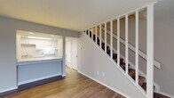 Located at 2400 Shore Blvd W. in Columbus, Ohio, this two-floor residence offers a well-organized layout designed for comfortable everyday living. The main level features an open living area finished with durable wood-look vinyl flooring and neutral gray walls, creating a clean, modern aesthetic throughout. A white-baluster staircase with carpet-covered treads anchors the space visually while providing access to the upper floor.

The kitchen is positioned adjacent to the living area and accessible via a pass-through peninsula with light granite-style countertops. White cabinetry lines the kitchen walls, complemented by a gas range and an under-cabinet range hood. The layout allows for easy interaction between the kitchen and living areas.

Upstairs, the bedrooms feature soft carpeting and neutral wall tones, with one bedroom offering access to a walk-in closet with built-in shelving. The full bathroom on this level includes a granite-topped vanity with an undermount sink, wood-look vinyl flooring, a skylight for natural light, and a full soaking tub with a shower surround. A textured ceiling is present in select areas of the home. Overall, the space presents a clean, updated interior with consistent finishes across both floors.