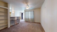 This single-floor residence offers a functional and comfortable layout across several well-defined living spaces. The main living area is generously sized, finished with wall-to-wall carpeting and anchored by a ceiling fan with integrated lighting. A large window dressed with patterned curtains allows natural light to fill the room, while a built-in bookshelf provides convenient storage and display space. A breakfast bar with bar-stool seating connects the living area to the kitchen, creating an open, social flow between the two spaces.

The galley-style kitchen is efficiently designed with light wood cabinetry, laminate countertops, a stainless steel sink, and white appliances including a refrigerator, electric range, and over-the-range microwave. Tile flooring and a doorway leading to additional storage complete the kitchen's practical setup.

The two bedrooms are carpeted and well-lit, each featuring windows with outdoor views of surrounding greenery. One bedroom includes a walk-in closet, while the other offers direct access to a full bathroom. Both bathrooms are tiled and equipped with a vanity, large mirror, ample cabinet storage, and a tub/shower combination, providing functional and comfortable everyday use throughout the residence.