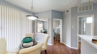 This single-floor residence is finished in a consistent cool gray palette throughout, creating a unified and contemporary aesthetic across all rooms. Hardwood-style flooring runs through the main living areas, hallways, and kitchen, while the bedroom transitions to plush carpet for added comfort.

The living room serves as a central gathering space, anchored by a tile-surround fireplace and complemented by a large sliding glass door that opens to an outdoor patio, allowing natural light to fill the room. A dedicated dining area sits adjacent, illuminated by a pendant light fixture and framed by vertical blinds.

The kitchen is well-equipped with white cabinetry, stone-look countertops, stainless steel appliances including a refrigerator, range, and microwave, and a peninsula with a built-in sink and pendant lighting overhead. A pass-through opening connects the kitchen visually to neighboring spaces.

The bedroom is generously sized with a textured ceiling and direct access to a bathroom featuring white cabinetry and stone-look countertops. The bathroom includes a tub-shower combination and continues the hardwood-style flooring. A hallway connects the bedroom, bathroom, and additional closet or utility access, completing the functional layout of this thoughtfully designed residence.