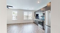 This thoughtfully designed one-bedroom, one-bathroom unit offers a clean, contemporary aesthetic throughout its efficiently arranged single floor. The open-concept kitchen and living area serves as the heart of the space, featuring light hardwood-style flooring, recessed lighting, and large windows that invite abundant natural light and views of the surrounding neighborhood. The kitchen is well-appointed with gray shaker-style cabinetry, striking navy blue subway tile backsplash, granite-look countertops, and a full suite of stainless steel appliances including a refrigerator, range, microwave, and dishwasher.

A bright hallway with a sliding barn door connects the main living area to the private bedroom, which features plush carpeting, a ceiling fan, and a walk-in closet with built-in shelving. The bathroom is finished with bold hexagonal dark tile flooring, a gray vanity with granite countertop, an illuminated LED mirror, and a tiled shower. Convenience is further enhanced by a dedicated in-unit laundry closet housing a stacked full-size washer and dryer. The overall design palette — crisp white walls, warm wood-tone floors, and modern fixtures — creates a cohesive, move-in-ready living environment.