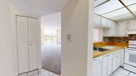 Located in Miami's Fontainebleau area, this single-floor unit at 8960 NW Eighth St offers a practical and well-organized layout. The living room is spacious and carpeted, featuring a large sliding glass door that opens to a private balcony with views of the surrounding landscape and water, allowing natural light to fill the room throughout the day. A textured ceiling and neutral wall tones give the living space a clean, understated appearance.

The kitchen is a dedicated, enclosed area finished with white tile flooring, white cabinetry, and warm wood-toned countertops. A mosaic tile backsplash with earth-toned accents provides a decorative touch. The kitchen is equipped with a white electric range, refrigerator, and a double sink, with ample cabinet storage above and below the counters. A drop ceiling with panel lighting brightens the workspace.

The bedroom is generously proportioned, also featuring carpet flooring and a window with natural light. It includes multiple closets — a louvered closet and an additional walk-in style closet — offering practical storage solutions. The bathroom features a full soaking tub with a tiled surround in warm beige tones, accented by a decorative mosaic border. The entry area transitions between tile and carpet, with a closet nearby. Overall, the unit presents a functional, light-filled layout suited to comfortable Miami living.