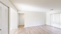This single-story, 2-bedroom, 1-bathroom residence offers a thoughtfully designed layout across a comfortable footprint. The interior is finished with light-toned wood-style flooring throughout the main living areas, complemented by crisp white walls and clean white baseboards that give the space a bright, airy feel.

The living areas are generously sized, with large sliding glass doors dressed in vertical blinds that invite natural light and provide views of the surrounding greenery. The kitchen is a functional highlight, featuring warm wood cabinetry, dark granite-style countertops, a kitchen island for additional prep space, recessed and flush-mount lighting, and black appliances including a gas range, dishwasher, and refrigerator. A dedicated in-unit stacked washer and dryer is conveniently tucked just off the kitchen.

The two bedrooms are carpeted for comfort, each offering vertical-blind-covered windows that filter natural light. The spacious primary bedroom includes a built-in closet with bifold doors and a dedicated rod and shelf system. The full bathroom is finished with large-format beige wall tiles in the tub/shower surround, wood-style flooring, a vanity with wood cabinetry, and a full bathtub. A hallway and additional closet provide practical storage throughout.