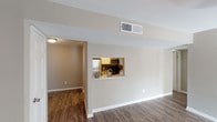 This single-floor unit offers a well-organized layout with a clear separation between living, kitchen, and sleeping areas. The living room serves as the central gathering space, finished with dark hardwood-style flooring that extends throughout the common areas. A sliding glass door fitted with vertical blinds allows natural light to fill the room, while a ceiling light fixture adds warmth overhead. A pass-through window connects the living area directly to the kitchen, creating an open, communicative flow between the two spaces.

The kitchen is efficiently designed with white cabinetry, granite-style countertops, a stainless steel sink, and stainless steel appliances including a refrigerator and microwave. A doorway from the kitchen leads further into the unit's interior hallway.

The bedrooms are carpeted and feature neutral taupe walls, window blinds for light control, and ceiling fan fixtures. Each room offers closet access and a calm, understated aesthetic well-suited for comfortable living.

Two bathrooms serve the unit. The primary bathroom includes a wide vanity with granite-style countertops, white cabinetry, and a well-lit mirror with a multi-bulb fixture above. The secondary bathroom features a full tub-shower combination with a window for natural ventilation. Both bathrooms continue the consistent use of hardwood-style flooring and clean white finishes throughout.