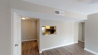 This single-floor unit offers a well-organized layout with a clear separation between living, kitchen, and sleeping areas. The living room serves as the central gathering space, finished with dark hardwood-style flooring that extends throughout the common areas. A sliding glass door fitted with vertical blinds allows natural light to fill the room, while a ceiling light fixture adds warmth overhead. A pass-through window connects the living area directly to the kitchen, creating an open, communicative flow between the two spaces.

The kitchen is efficiently designed with white cabinetry, granite-style countertops, a stainless steel sink, and stainless steel appliances including a refrigerator and microwave. A doorway from the kitchen leads further into the unit's interior hallway.

The bedrooms are carpeted and feature neutral taupe walls, window blinds for light control, and ceiling fan fixtures. Each room offers closet access and a calm, understated aesthetic well-suited for comfortable living.

Two bathrooms serve the unit. The primary bathroom includes a wide vanity with granite-style countertops, white cabinetry, and a well-lit mirror with a multi-bulb fixture above. The secondary bathroom features a full tub-shower combination with a window for natural ventilation. Both bathrooms continue the consistent use of hardwood-style flooring and clean white finishes throughout.
