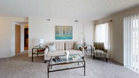 Wyndham Ridge presents a thoughtfully designed single-floor residence that balances comfort and functionality throughout its living spaces. The living room is generously sized, featuring plush carpeting, a textured ceiling, and a large sliding glass door with vertical blinds that allows for ample natural light. An adjacent dining area provides an intimate setting, accented by decorative wall art and a glass-top table. The kitchen is well-equipped with warm oak cabinetry, white appliances including a refrigerator and dishwasher, a double-basin sink, and durable hardwood-style flooring that adds contrast to the neutral tones throughout. The primary bedroom is a comfortable retreat, complete with a ceiling fan, soft carpeting, a walk-in closet, and a window dressed with light curtains. A secondary bedroom functions well as a home office or guest room, featuring a bright window and generous floor space. The primary bathroom includes a standalone walk-in shower with a chrome-framed glass door, while the secondary bathroom features a wood-vanity, a large mirror, and convenient in-unit laundry access. Throughout the home, neutral wall tones and consistent carpeting create a cohesive, welcoming atmosphere.