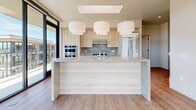 This contemporary 3-bedroom, 2-bathroom residence in Lehi, Utah, offers a sleek, modern design defined by clean lines, warm wood-look flooring throughout, and an abundance of natural light. The open-concept living area is anchored by dramatic floor-to-ceiling glass walls that frame sweeping panoramic views of the surrounding mountains and cityscape, creating a bright and airy atmosphere that seamlessly blends indoor and outdoor living.

The gourmet kitchen is a standout feature, appointed with light wood cabinetry, stone countertops, a large waterfall-edge island, stainless steel appliances including a double wall oven and gas cooktop, and three statement pendant lights overhead. A skylight adds additional natural illumination to this well-appointed culinary space.

The spacious primary bedroom includes access to an outdoor balcony through sliding glass doors, while the en-suite bathroom impresses with dual vanities featuring stone countertops, a soaking tub, a separate glass-enclosed shower, and a floor-to-ceiling window offering mountain views. The second bathroom mirrors the refined aesthetic with a tiled tub-shower combo and a sleek wood-framed vanity with illuminated mirror.

Additional bedrooms are well-sized, each outfitted with track lighting, and the home includes two closets and a clean, modern hallway connecting all spaces cohesively.