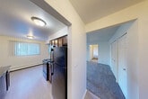 Located at 5216 Perry Rd in Grand Blanc, Michigan, this single-floor, 2-bedroom, 1-bathroom home offers a functional and comfortable layout. The entrance opens into a hallway that connects all main areas of the home, with plush carpeting running through the living spaces and easy-care hard flooring in the kitchen and dining areas.

The combined kitchen and dining area is a practical highlight of the home. The galley-style kitchen features rich dark wood cabinetry, dark granite countertops, black appliances including a refrigerator, electric range with microwave, and dishwasher, offering ample storage and prep space. A window with vertical blinds brings in natural light to the adjacent dining area.

The living room provides a comfortable gathering space, while the carpeted hallway leads to two well-sized bedrooms. The spacious primary bedroom includes wall-mounted air conditioning and access to the bathroom, while the second bedroom features a large window overlooking greenery, filling the room with natural light. Both rooms are served by abundant closet space — a total of five closets throughout the home.

The full bathroom is tastefully finished with large-format travertine tile surrounding the tub and shower, dark granite countertops on the wood vanity, a large mirror, and neutral tile flooring. Baseboard heating is present throughout the home, ensuring comfort year-round.