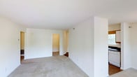 This single-floor residence features one bedroom and one bathroom, offering a practical and easy-to-navigate layout. The living area is finished with wall-to-wall carpet in a neutral tone, providing a soft, comfortable underfoot feel throughout the space. Crisp white walls and a textured ceiling keep the aesthetic clean and bright, creating a blank canvas that adapts well to a variety of furnishing styles. A doorway leads from the main living area into the adjoining hallway or bedroom, hinting at a connected and efficiently designed floor plan. The transition between spaces is smooth, with consistent flooring and finishes tying the rooms together cohesively. The overall ambiance is simple and move-in ready, with minimal visual clutter allowing the functional layout to take center stage. Natural light contributes to a bright interior atmosphere, enhancing the openness of the living space. The straightforward design makes the most of the available square footage, offering comfortable single-floor living suited for individuals or couples seeking a low-maintenance, easy-to-maintain home.