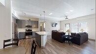 This single-floor unit showcases a thoughtfully designed open-concept layout that seamlessly connects the kitchen, dining, and living areas. The kitchen is a standout feature, equipped with slate-gray shaker-style cabinetry, quartz countertops, stainless steel appliances including a range, microwave, dishwasher, and refrigerator, and a central island with pendant lighting overhead. Wood-look flooring extends throughout the main living areas, adding warmth and visual continuity.

The dining area includes a built-in desk nook with matching gray cabinetry, offering a practical workspace alongside the dining table. The living room benefits from generous natural light streaming through large windows fitted with vertical blinds, a ceiling fan, and an electric fireplace that adds a cozy focal point to the space.

The bedrooms are carpeted and comfortably sized, each featuring ceiling fans. One bedroom includes a walk-in closet, while another accommodates twin beds and receives ample natural light. Two bathrooms are present, both featuring gray vanity cabinetry, quartz countertops, and shower-tub combinations, maintaining the unit's consistent modern aesthetic throughout.