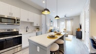 Located at 1500 Westshore Dr in Cumming, GA, this thoughtfully designed single-floor residence combines modern aesthetics with functional living. The open-concept kitchen is a standout feature, showcasing white shaker cabinetry, a subway tile backsplash, stainless steel appliances, a matte black faucet, and a spacious central island with bar seating, all illuminated by bold black dome pendant lights. The kitchen flows seamlessly into the living area, where light wood-look flooring, neutral gray walls, and large windows with French doors invite an abundance of natural light and outdoor views. The living room offers a relaxed yet refined atmosphere, complemented by a wall-mounted TV, built-in media storage, and access to an outdoor area. A dedicated workspace nook with built-in shelving provides a practical retreat. The bedrooms are serene and comfortable, featuring plush carpeting, generous windows, and soft neutral tones. The bathroom is finished with gray cabinetry, a white countertop, wood-look flooring, and a walk-in closet nearby. Throughout the residence, black hardware accents provide a consistent, contemporary design thread, creating a cohesive and inviting home.