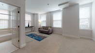 Located at 101 W Read St in Baltimore's vibrant Mount Vernon neighborhood, this single-floor residence offers a well-designed layout that balances comfort and functionality. The open living area is filled with natural light streaming through multiple windows fitted with clean white blinds, creating a bright and airy atmosphere. Neutral carpet flooring and soft gray walls lend the space a calm, cohesive feel throughout.

The kitchen is thoughtfully designed with a peninsula breakfast bar seating two, dark granite-style countertops, warm wood cabinetry, and black appliances including a range and full-size refrigerator. Rich hardwood flooring anchors the kitchen area, adding a warm contrast to the surrounding carpeted spaces.

The bedroom is generously proportioned, featuring multiple sets of bifold closet doors that offer exceptional storage capacity. A patterned area rug and dual windows bring character and natural light to the room. An additional secondary bedroom or flex room also benefits from multiple windows and a bright, open feel.

The bathroom showcases classic square tile work throughout, with a deep soaking tub positioned beneath a window that allows natural light to filter in, enhancing the clean, timeless aesthetic. The overall ambiance of this residence is welcoming and practical, making it a comfortable urban retreat in the heart of Baltimore.