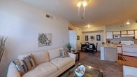 Located at 910 Wooded Creek Dr in Cedar Hill, Texas, this single-story residence offers a well-organized layout designed for comfortable everyday living. The open-concept living area is anchored by neutral-toned carpet and features a decorative chandelier overhead, with natural light filtering in through a large window dressed with sheer curtains. The space flows seamlessly into a defined dining area, which accommodates a round table for four and is accented by framed wall art and a geometric mirror, creating an intimate yet connected atmosphere.

The kitchen is equipped with ample wood-trimmed cabinetry, tile and hardwood-style flooring, a electric range, built-in microwave, and a peninsula breakfast bar that bridges the kitchen and living spaces. Track lighting illuminates the area effectively.

The primary bedroom is a calm retreat with carpeted flooring, a ceiling fan, and a wide window allowing natural light. It is served by a full bathroom featuring a double-sink vanity with extended cabinetry and hardwood-style flooring. An additional bedroom offers comfortable proportions with a ceiling fan and natural light, suitable as a guest or children's room. A second full bathroom with a tub-shower combination and hardwood-style flooring serves the remaining bedrooms.