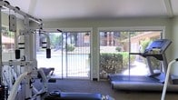 This single-floor fitness room is designed to provide a functional and well-lit workout environment. The space is equipped with a multi-station strength training machine, a treadmill, and additional free weights, offering a well-rounded selection of exercise options for residents or guests.

One of the standout features of this fitness room is its wall of large sliding glass doors, which flood the interior with abundant natural light and create a seamless visual connection to the outdoors. Through the doors, views extend directly to an outdoor swimming pool and a neatly landscaped courtyard surrounded by mature trees and shrubs, lending the space an open and airy atmosphere despite its compact footprint.

The interior finishes are clean and practical, with neutral-toned walls and low-maintenance flooring suited for a high-activity environment. The layout is straightforward and efficient, allowing for easy movement between equipment. A no-smoking sign is posted near the entrance, indicating a clearly defined wellness-focused policy for the space.

Overall, this fitness room combines essential workout amenities with pleasant outdoor views, making it a convenient and inviting option for those looking to maintain an active lifestyle on-site.