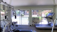 This single-floor fitness room is designed to provide a functional and well-lit workout environment. The space is equipped with a multi-station strength training machine, a treadmill, and additional free weights, offering a well-rounded selection of exercise options for residents or guests.

One of the standout features of this fitness room is its wall of large sliding glass doors, which flood the interior with abundant natural light and create a seamless visual connection to the outdoors. Through the doors, views extend directly to an outdoor swimming pool and a neatly landscaped courtyard surrounded by mature trees and shrubs, lending the space an open and airy atmosphere despite its compact footprint.

The interior finishes are clean and practical, with neutral-toned walls and low-maintenance flooring suited for a high-activity environment. The layout is straightforward and efficient, allowing for easy movement between equipment. A no-smoking sign is posted near the entrance, indicating a clearly defined wellness-focused policy for the space.

Overall, this fitness room combines essential workout amenities with pleasant outdoor views, making it a convenient and inviting option for those looking to maintain an active lifestyle on-site.