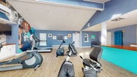 Located at 828 Orienta Ave in Altamonte Springs, Florida, this fitness center is a thoughtfully designed, single-floor facility built to support a comprehensive workout experience. The space is defined by its striking blue walls accented with teal and white trim, creating an energizing atmosphere that motivates activity. Light wood-style flooring runs throughout, adding warmth and easy maintainability underfoot.

The cardio zone is generously outfitted with multiple treadmills, elliptical trainers, and recumbent bikes from reputable brands including Life Fitness and Spirit, providing options for users of all fitness levels. A dedicated free weight area features a multi-tier dumbbell rack, while a functional training section includes medicine balls, kettlebells, stability balls, and resistance equipment neatly organized on racks and countertops with rich wood surfaces.

Natural light enters through several windows fitted with blinds and a skylight, brightening the space during daytime hours. Large glass sliding doors on one side offer views of the outdoors. Bold motivational murals and framed artwork adorn the walls, contributing to an upbeat, gym-like ambiance. Built-in white cabinetry provides additional storage throughout. The facility is well-ventilated, clearly marked with safety signage, and designed to accommodate a variety of fitness routines in a clean, open environment.