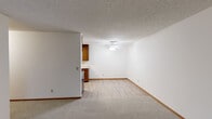 This single-floor unit offers a practical and comfortable layout designed for everyday living. The living area is carpeted and bathed in natural light from a large sliding glass door that opens to a view of lush greenery, complemented by vertical blinds and a ceiling fan overhead. The textured ceilings and warm wood baseboards carry throughout, creating a cohesive and consistent aesthetic.

The galley-style kitchen is efficiently designed, featuring rich warm-toned wood cabinetry that extends to the upper walls for ample storage. Light laminate countertops provide workspace alongside a double-basin sink, a stainless steel refrigerator, a range with coil burners, and a built-in microwave. A skylight-style overhead fixture illuminates the kitchen, and the space transitions seamlessly into an adjacent dining or hallway area.

The entry area includes a set of warm wood sliding closet doors offering generous storage. The full bathroom is clean and functional, showcasing a wood vanity with a white sink, a wide mirror, a toilet, and a full tub-shower combination. The floor features a classic two-tone tile pattern in neutral tones.

A bedroom with soft carpeting, neutral walls, and warm wood trim completes the layout, offering a quiet and comfortable retreat. Overall, the unit presents a well-maintained, functional living space with consistent warm-toned finishes throughout.