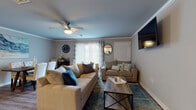 This single-floor residence offers a thoughtfully designed layout with a comfortable blend of modern finishes and functional living spaces. The living room serves as the heart of the home, featuring crown molding, a ceiling fan, and large sliding glass doors that invite natural light and provide access to the outdoors. Two plush sofas and a rustic wood coffee table create a warm, inviting atmosphere. The kitchen is a standout feature, showcasing white shaker cabinetry, dark granite-style countertops, a mosaic tile backsplash, and stainless steel appliances including a gas range and French door refrigerator. A generously sized island with seating for four anchors the space, making it ideal for both cooking and casual dining. Wood-look flooring flows throughout the main areas, adding warmth and continuity. The bedrooms are carpeted for comfort, each equipped with a ceiling fan and ample room for furnishings. Two bathrooms serve the home — one with a soaking tub and shower combination, and another with a walk-in shower — both finished with wood-look flooring and neutral gray walls. A dedicated laundry room houses a full-size washer and dryer with overhead wire shelving for added storage, completing this well-rounded and move-in-ready home.