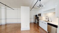 Located at 117 E 6th Street in the heart of Downtown Los Angeles, this single-floor urban loft blends industrial character with modern finishes. The open-concept layout is anchored by gleaming polished terracotta-toned tile flooring that flows seamlessly throughout the space, reflecting light and adding warmth to the clean, white surroundings.

Soaring ceilings with exposed black track and pipe railing systems lend an industrial aesthetic while accommodating a striking sputnik-style chandelier that serves as a focal design element. The kitchen is fully equipped with stainless steel appliances — including a range, microwave, refrigerator, and dishwasher — complemented by sleek white cabinetry, marble-look backsplash, and a deep basin sink with a modern faucet. A partial wall divider subtly delineates the kitchen and living areas while preserving the open, airy feel.

The main living area is generously proportioned and bathed in natural light through large, multi-pane windows fitted with horizontal blinds, offering views of the surrounding urban streetscape. The bathroom features classic penny tile flooring, a floating white vanity with a large mirror, and bright windows that enhance the clean, minimalist aesthetic. This loft is an ideal canvas for city living in one of LA's most vibrant neighborhoods.