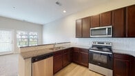 Located at 8891 Moreland St in Powell, Ohio, this single-floor residence offers a thoughtfully designed layout that balances functionality and comfort. The kitchen serves as a central highlight, showcasing rich dark-stained cabinetry, granite countertops, a classic white subway tile backsplash, and a full suite of stainless steel appliances including a range, microwave, dishwasher, and refrigerator. Light wood-style flooring runs throughout the kitchen and connecting areas, contributing to a clean, contemporary aesthetic. A raised peninsula counter separates the kitchen from the adjoining living area, creating an open-concept flow ideal for everyday living and entertaining. The living space is carpeted and bathed in natural light from large windows fitted with horizontal blinds, offering views of the surrounding outdoor greenery. The bedroom continues the warm, neutral palette with plush carpet and a generously sized window that invites ample daylight. The bathroom features a full tub-shower combination with built-in shelving, a toilet, and wood-style flooring, all finished in crisp white and neutral tones for a clean, functional feel. Throughout the unit, neutral wall colors and consistent finishes create a cohesive and inviting atmosphere.
