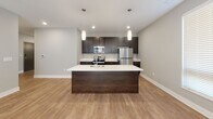 This single-floor residence offers a well-designed layout that balances open communal spaces with private retreats. The kitchen serves as a central focal point, showcasing dark espresso cabinetry paired with crisp white countertops and a full suite of stainless steel appliances, including a refrigerator, microwave, and range. A generously sized kitchen island with pendant lighting above provides additional workspace and a natural gathering point that flows seamlessly into the living area. The living room benefits from multiple windows dressed with horizontal blinds, allowing natural light to fill the space, which is finished with warm wood-look vinyl plank flooring.

The two bedrooms are carpeted for comfort, each equipped with a ceiling fan and windows that bring in natural light. Both bathrooms are finished consistently with dark cabinetry, white countertops, and wood-look flooring. One bathroom features a tub-shower combination, while the second offers a shower with a clean, minimalist vanity and mirror. The entryway and hallways feature the same wood-look flooring, neutral gray walls, and white panel doors, creating a cohesive and modern aesthetic throughout the unit.