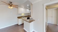 Located at 4351 Boardwalk Dr in Huntington Beach, California, this single-floor residence offers a clean, well-maintained layout with a cohesive design throughout. The kitchen serves as a functional centerpiece, featuring white shaker-style cabinetry with ample storage, rich granite countertops, a peninsula breakfast bar, and black appliances including an electric range, built-in microwave, and dishwasher. Recessed lighting illuminates the space, which flows seamlessly over dark hardwood-style flooring into the adjoining living area. Crown molding adds a refined architectural touch visible throughout the unit, complemented by textured ceilings. The living area is bright and open, benefiting from a full-width sliding glass door dressed with vertical blinds that invites generous natural light and provides access to an outdoor view. Carpeted bedroom spaces offer a softer, comfortable feel, with one room featuring its own sliding glass door access. The bathroom is appointed with granite countertops consistent with the kitchen, white cabinetry, a tub-shower combination, and hardwood-style flooring. Neutral wall tones and clean white trim throughout create a light, airy ambiance well-suited to the coastal Huntington Beach setting.