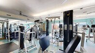 Located at 1333 Old Spanish Trail in Houston, TX, this fitness center offers a spacious, single-floor layout designed to accommodate a comprehensive range of workout activities. The facility is divided into two primary areas: a main strength and cardio training floor and a dedicated cycling studio.

The main workout area features light teal accent walls, rubberized flooring, and abundant natural light streaming through large sliding glass doors that open to views of the surrounding cityscape. Ceiling fans throughout help maintain a comfortable environment. The space is outfitted with a full suite of Magnum strength machines, free weights including a rack of dumbbells, benches, and cardio equipment such as treadmills and rowing machines. Wall-mounted TVs and full-length mirrors add to the functional design, while framed artwork contributes a polished aesthetic.

The cycling studio is a bright, dedicated room featuring warm bamboo hardwood flooring, floor-to-ceiling mirrors along one wall, and multiple ceiling fans. A full row of stationary spin bikes, stability balls, and wall-mounted flat-screen TVs make this space ideal for group fitness classes or individual cycling sessions.

Together, the two areas form a well-rounded fitness facility that balances functionality with a clean, modern design.