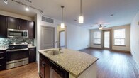 This single-floor residence offers a thoughtfully designed open-concept layout that seamlessly connects the kitchen, dining, and living areas. The kitchen is a standout feature, showcasing rich dark cabinetry, stainless steel appliances including a refrigerator, range, and microwave, a decorative mosaic tile backsplash, and a large granite-topped island with an undermount sink and pendant lighting overhead. Hardwood flooring runs throughout the main living areas, adding warmth and continuity, while a ceiling fan and access to an outdoor balcony enhance the living room's comfort and natural light.

The bedrooms are carpeted and bright, each featuring ceiling fans and windows with blinds that allow ample natural light. The layout accommodates multiple bedrooms, providing flexible living arrangements.

Both bathrooms are finished with consistent, high-quality details including granite vanity countertops, dark wood cabinetry, framed mirrors, and light tile flooring. The primary bathroom includes a walk-in closet with built-in shelving, offering generous storage. The secondary bathroom mirrors the same refined aesthetic with additional wall-mounted cabinetry.

Overall, the space presents a cohesive modern design with a neutral color palette, quality finishes throughout, and a functional floor plan suited for comfortable everyday living.