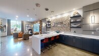 Located at 214 Bellemeade St in Greensboro, NC, this single-floor space serves as the Carroll Bellemeade leasing office and showcases a thoughtfully designed, contemporary interior. Polished concrete flooring flows throughout, anchoring the open, modern aesthetic across every area.

The dual kitchen areas are a standout feature, centered around a bold, oversized accent wall clad in stacked raw wood cross-sections bearing the Carroll Bellemeade name. Navy blue cabinetry with crisp white quartz countertops lines the kitchen, while a large white island with bar seating and pendant globe lighting creates an inviting, social atmosphere. Open floating shelves display curated décor, and a beverage refrigerator adds functional elegance.

A dedicated wine lounge offers an intimate retreat, featuring a live-edge wood communal table, leather seating, dark wood cabinetry with stemware storage, a wine cooler, and a stacked stone accent wall bearing a bold "Wine Lounge" sign.

The living room provides a comfortable gathering space, highlighted by large street-facing windows dressed in floor-length drapes that invite natural light and neighborhood views. A reclaimed wood accent wall frames a large video display, while curated artwork and sophisticated furnishings complete the refined ambiance. The office and hallway connect the spaces efficiently, making this a well-appointed, detail-rich environment.