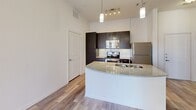 Located at 1100 South Boulevard in Charlotte's vibrant South End neighborhood, this one-bedroom, one-bathroom residence offers a well-designed single-floor layout with a thoughtful mix of modern finishes and functional spaces. The kitchen serves as a central highlight, featuring dark cabinetry, granite countertops, stainless steel appliances including a refrigerator, range, and built-in microwave, and a curved peninsula with a double undermount sink. Pendant lighting above the peninsula adds a contemporary touch, while wood-look flooring extends throughout the main living and kitchen areas, creating a cohesive and clean aesthetic. The bedroom is generously sized, finished with plush carpet, a ceiling fan, and a window that allows natural light to filter in. A spacious walk-in closet with multi-level wire shelving connects directly to the bedroom, providing ample storage. The full bathroom is well-appointed with dark vanity cabinetry, a marble-style countertop, a framed mirror with vanity lighting, and a tub-shower combination, all set on wood-look tile flooring. A dedicated in-unit laundry area with side-by-side washer and dryer hookups adds everyday convenience. The overall ambiance is clean, contemporary, and move-in ready.