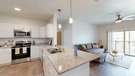 Located at 6834 Milwaukee St in Madison, WI, this 2-bedroom, 3-bathroom unit offers a well-designed, single-floor layout with modern finishes throughout. The open-concept kitchen and living area serves as the heart of the home, anchored by a granite-topped island with a double sink and elegant pendant lighting. White shaker cabinetry, stainless steel appliances, and wood-look luxury vinyl flooring complete the kitchen, which flows naturally into the bright, comfortable living room. The living room features a ceiling fan, sliding glass door access to a private balcony with outdoor views, and large windows that invite natural light. The bedrooms are carpeted for comfort; the primary bedroom includes a spacious walk-in closet with built-in shelving and sliding doors. The three bathrooms maintain consistent styling with granite vanity tops, white cabinetry, and wood-look flooring. One bathroom offers an extended layout with a shower and ample towel storage. Additional highlights include a dedicated utility room, a separate closet for storage, and a clean, neutral color palette throughout that gives the space a bright, contemporary feel.