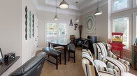 Located along Primrose Parkway in Johns Creek, Georgia, this single-floor community space combines functionality with a lively, eclectic aesthetic. The interior is finished with neutral warm-toned walls, crown molding, and tray ceiling details that lend an architectural elegance to the room. Patterned carpeting in earthy tones runs throughout, anchoring the space with warmth and texture.

Industrial-style pendant lights hang from the ceiling, casting a welcoming glow over distinct functional zones. A dedicated business center area features a computer workstation with an ergonomic chair and printer, making it well-suited for productivity needs. Adjacent to this is a conference or meeting area with a dark wood table and seating, ideal for small gatherings or collaborative work.

A lounge area is furnished with bold, multi-striped wingback chairs that serve as a visual focal point, complemented by eclectic décor including decorative wall art, twig arrangements, and whimsical signage. A rustic, colorfully painted sideboard holds a coffee and beverage station, adding a hospitality-forward touch.

Large windows along one wall allow natural light to filter in, offering views of the lush outdoor surroundings. A standout feature is a classic red popcorn machine, adding a playful and social element to the space. Overall, the area balances comfort, practicality, and personality in a distinctive community setting.