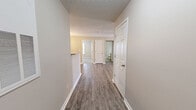 Located at 8027 Glimmer Way in Louisville, Kentucky, this single-floor, 3-bedroom, 2-bathroom home offers a practical and well-organized layout. The galley-style kitchen is outfitted with light wood cabinetry, a double-basin sink, a full suite of white appliances including a refrigerator and electric range, and a peninsula that opens toward the dining area. A elegant chandelier accents the adjacent dining space, which flows naturally into the main living area. The living room features durable wood-look plank flooring and a ceiling fan, providing a comfortable, open feel. The three bedrooms are finished with plush carpeting and neutral wall tones, with windows in the secondary bedrooms bringing in natural light. The primary bedroom offers a generous footprint relative to the overall layout. Both bathrooms are appointed with light wood vanities, tile flooring, and a full tub-shower combination. A dedicated laundry room with wire shelving and electrical connections adds everyday convenience, while a central hallway efficiently connects all areas of the home. The textured ceilings and clean white trim throughout lend a consistent, cohesive aesthetic to the entire space.
