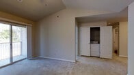 This single-floor residence offers a clean and functional layout designed for comfortable everyday living. The main living area immediately draws attention with its vaulted ceiling, which adds a sense of openness and airiness to the space. Soft, neutral-toned carpet flooring runs throughout, providing a warm and inviting underfoot feel that complements the room's understated, neutral color palette on the walls. A ceiling fan fixture is installed overhead, offering both lighting and climate comfort. Natural light filters into the space through a window, brightening the interior with a calm, diffused glow. One of the standout practical features of this residence is the in-unit laundry area, thoughtfully integrated into a dedicated closet alcove. The bi-fold closet doors open to reveal a side-by-side washer and dryer, keeping laundry needs contained and accessible without sacrificing living space. An adjacent door leads further into the residence, suggesting additional rooms beyond the main living area. The overall ambiance of the space is calm and neutral, presenting a versatile canvas well-suited to a variety of furnishing styles and personal tastes. Clean lines, practical storage, and thoughtful amenities make this a highly functional and livable single-floor home.