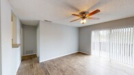 This single-story space is thoughtfully laid out to maximize functionality across its living areas. The main living room is a standout feature, showcasing durable wood-look flooring that extends throughout the primary living areas, neutral gray walls, and a ceiling fan with integrated lighting that promotes airflow and comfort. Vertical blinds frame a sliding glass door, allowing natural light to filter in while providing access to the outdoors.

The entryway transitions seamlessly from tile flooring into the wood-look flooring of the main living space, with a pendant light overhead and a nearby kitchen that is visible from the entry. The galley-style kitchen is well-equipped, featuring white cabinetry, dark countertops, a stainless steel sink, and black appliances including an electric range, refrigerator, and dishwasher. Light tile flooring completes the kitchen's clean aesthetic.

The bedroom offers plush carpeting underfoot and a window fitted with horizontal blinds, providing natural light and outdoor views. The bathroom includes a full tub-shower combination with white surrounds and tile flooring, maintaining a clean and functional design. Textured ceilings are consistent throughout the space.