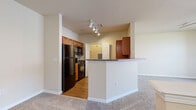This single-floor residence offers a thoughtfully designed layout that balances functionality and comfort throughout. The open-concept living and kitchen area serves as the heart of the home, where plush carpeting in the living space transitions to warm hardwood-style flooring in the kitchen. The kitchen is well-equipped with warm oak cabinetry, granite-style countertops, black appliances including a refrigerator, stove, and built-in microwave, and a peninsula that provides additional prep space and a natural divide between the two areas. Track lighting illuminates the kitchen, while a utility closet with a breaker panel adds practical convenience nearby. The living area is generously proportioned, featuring a ceiling fan and recessed lighting, with views into the kitchen peninsula creating an airy, connected feel. The bedroom features large windows fitted with blinds that invite abundant natural light and offer views of the surrounding neighborhood, complemented by a ceiling fan overhead. A spacious walk-in closet with built-in shelving provides excellent storage. The bathroom is finished with oak cabinetry, granite countertops, a framed mirror, hardwood-style flooring, and a full tub-shower combination with white tile surround, completing this comfortable and practical residence.